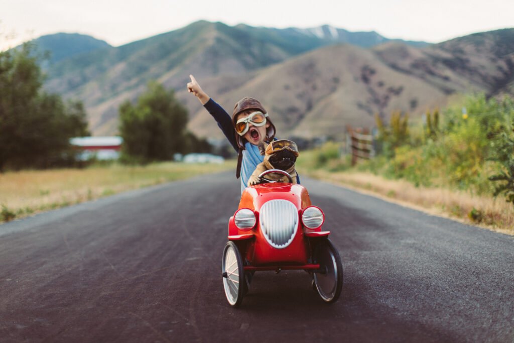 A boy & his dog race down the road in a red toy car